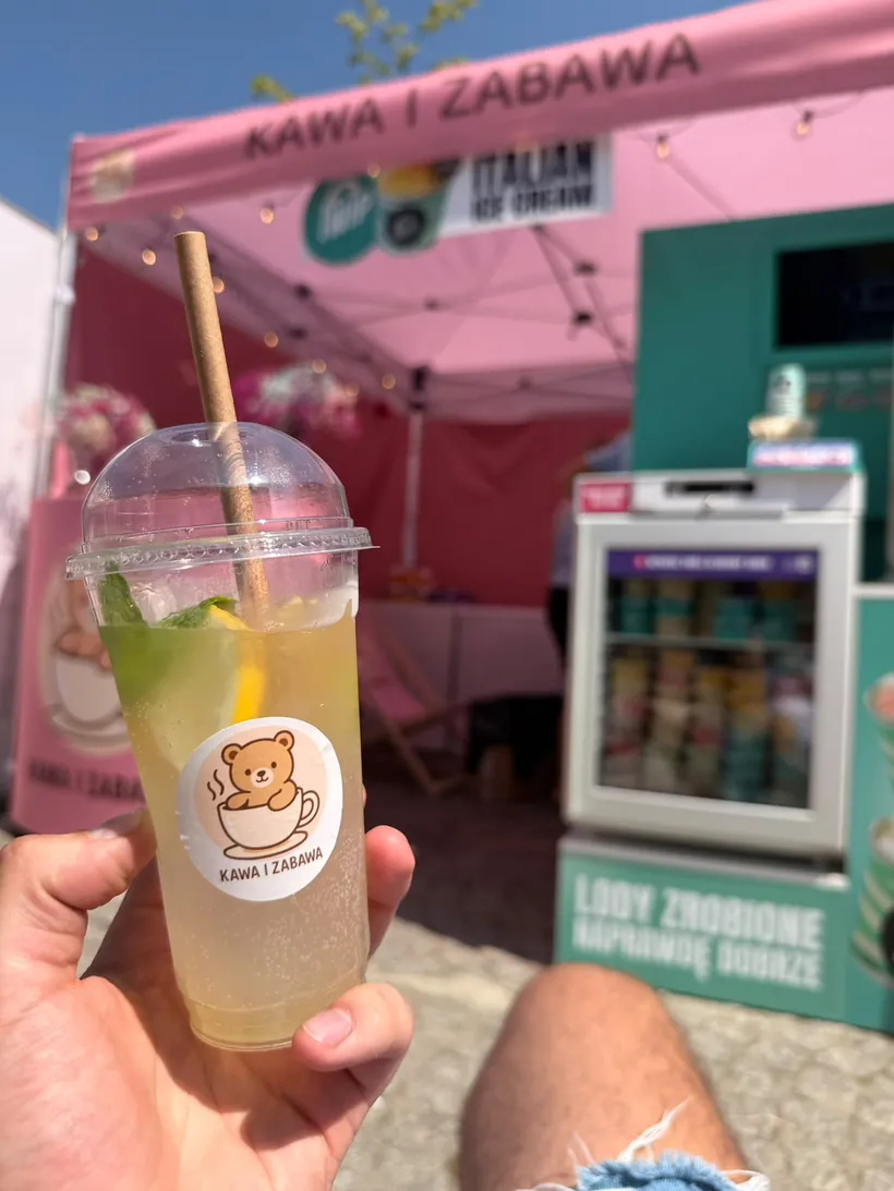 Lemoniada w kubku z logo Kawy i Zabawy, w tle stoisko z lodami fwip